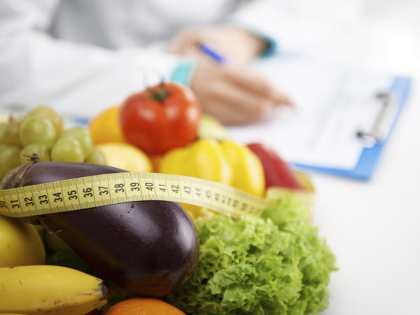 Healthy nutrition concept. Close-up of fresh vegetables and fruits with measuring tape lying on doctor's desk.