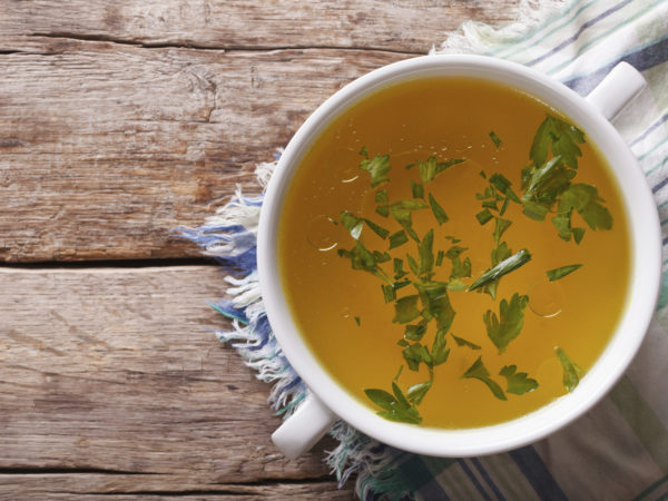 Tasty meat broth with parsley in a white bowl closeup. horizontal view from above