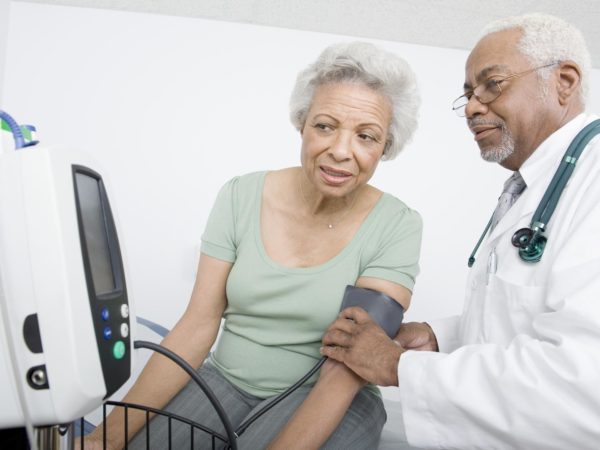 Male doctor checking patient's blood pressure while looking at machine at clinic