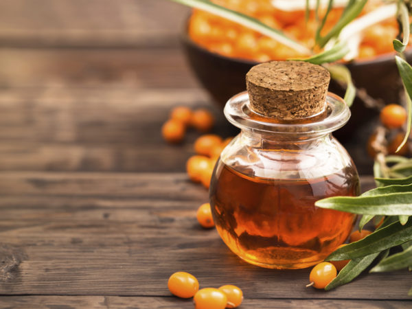 Sea buckthorn oil and branch with berries at right side of wooden background