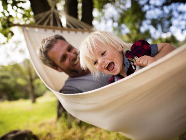 Lovely modern dad enjoys the outdoors playing with his son on a white hammock