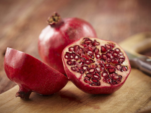 Sliced pomegranate on cutting board with knife and whole pomegranate behind. Shot with shallow focus on sliced fruit.