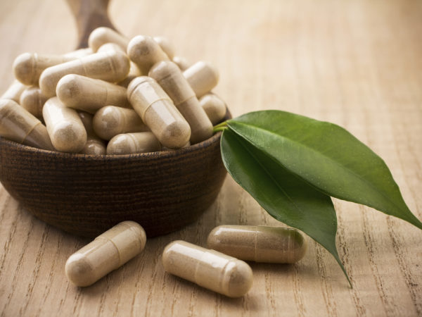 "Alternative medicine tablets on a wooden spoon, green leaf."